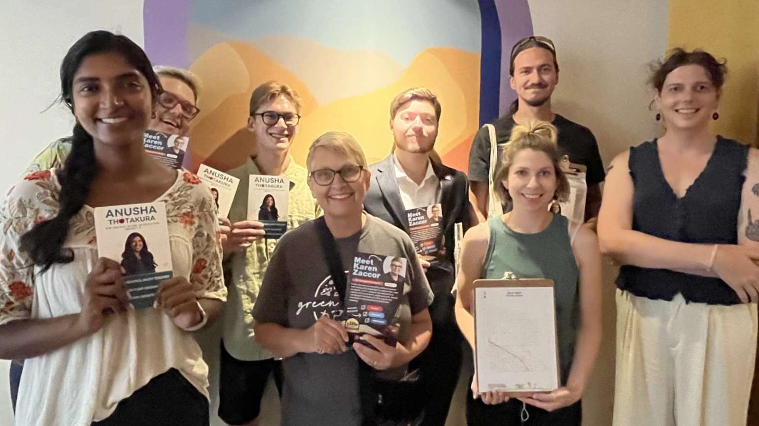 A group of people posing in two rows and facing the camera, smiling. Some of them are holding up canvassing literature that says "Anusha," others are holding different literature that says, "Karen Zaccor." Karen is in the middle of the front row.