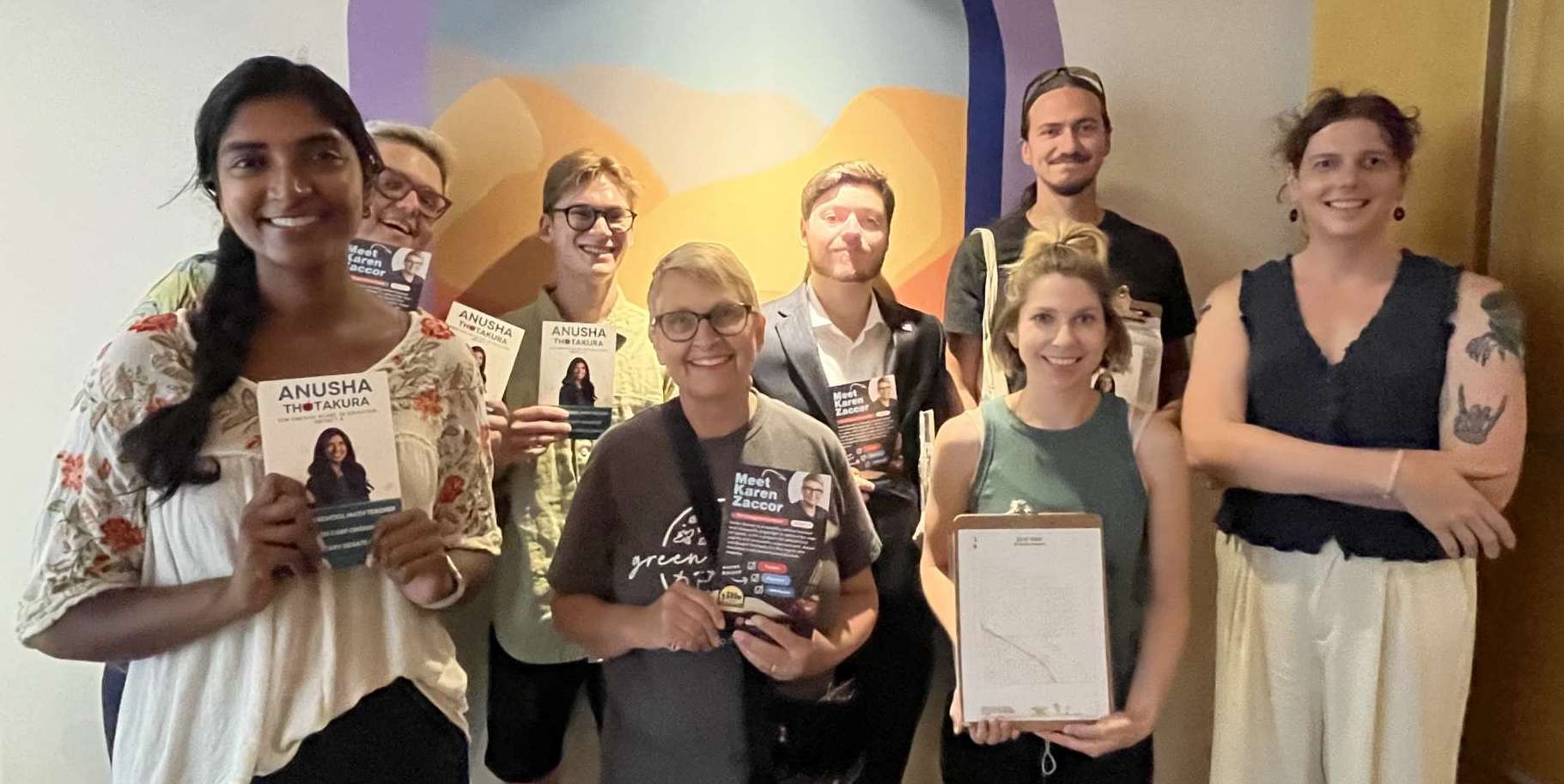 A group of people posing in two rows and facing the camera, smiling. Some of them are holding up canvassing literature that says "Anusha," others are holding different literature that says, "Karen Zaccor." Karen is in the middle of the front row.